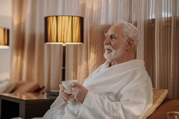 Grauhaariger älterer Mann, der Morgenkaffee trinkt und nachdenklich aussieht