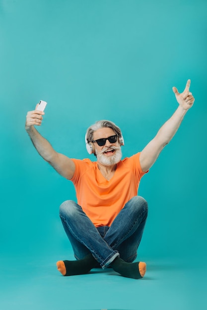 Grauhaariger älterer Mann mit Sonnenbrille posiert mit einem Telefon Studio-Shooting