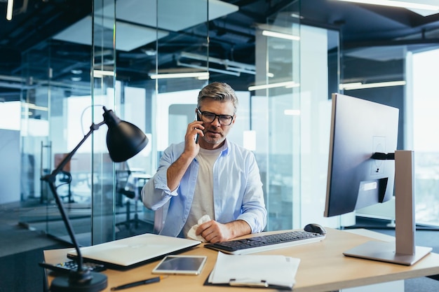 Grauhaariger Geschäftsmann mit laufender Nase, der im Büro am Computer arbeitet, Erkältung und Grippe