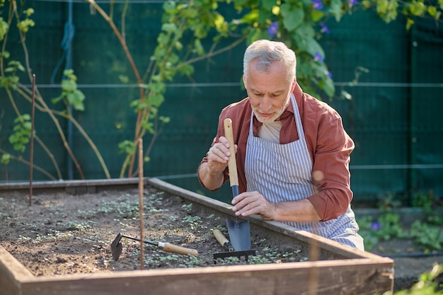 Grauhaariger Mann, der beschäftigt aussieht, während er im Garten arbeitet