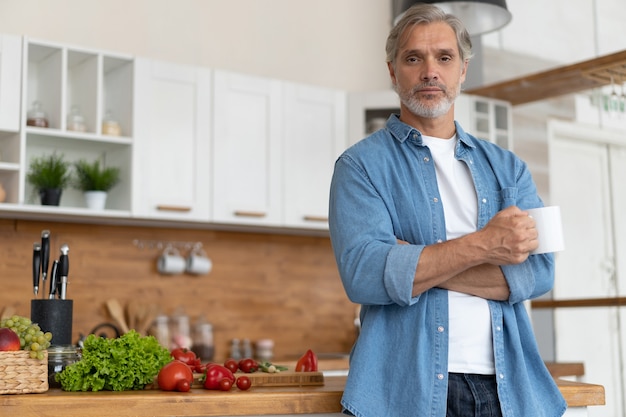 Grauhaariger Reifer hübscher kaukasischer Mann, der in der hellen Küche steht.