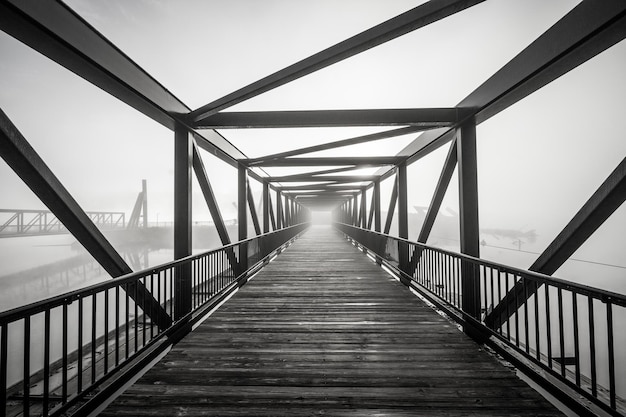 Graustufen-Lichtaufnahme am Ende einer modernen, wunderschön gestalteten Brücke, umgeben von Nebel