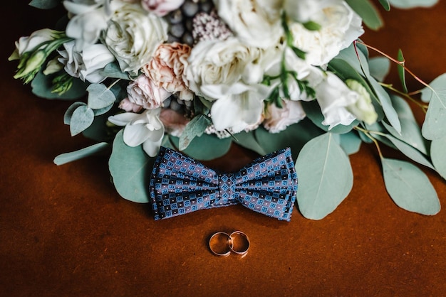 Gravata e anéis masculinos elegantes para noivo e noiva em um fundo de um buquê de flores Acessórios de casamento em fundo rústico de madeira marrom Composição da ideia Close up Vista superior