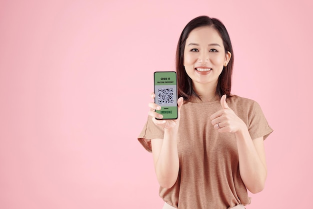 Grave boa jovem asiática mostrando smartphone com código QR, o que significa que ela foi vacinada