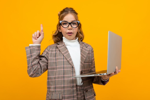 Grave colegiala caucásica inteligente con gafas en un traje de negocios y una chaqueta con una computadora portátil en sus manos en naranja
