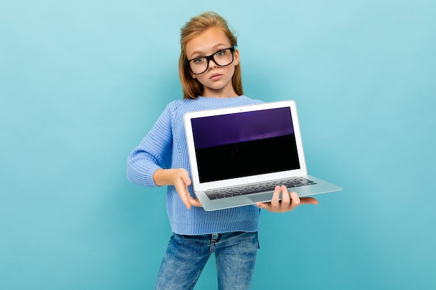 Grave colegiala elegante en vasos con una computadora portátil sobre un fondo de pared azul