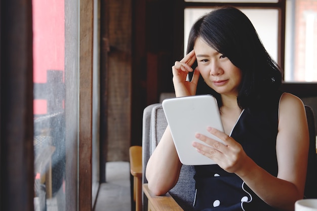 Foto grave empresaria asiática está leyendo y tiene dolor de cabeza con noticias en línea en tableta en la oficina moderna. concepto de tecnología y salud.