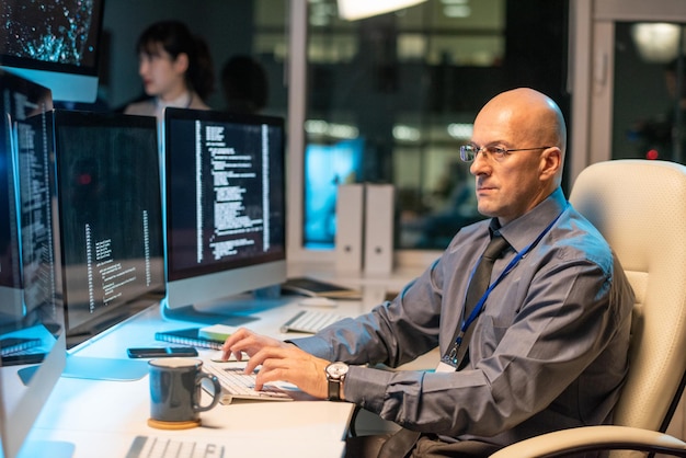 Grave empresario Calvo mirando a través de datos en la pantalla del ordenador