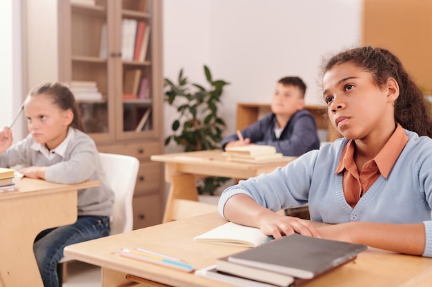 Grave estudiante de raza mixta de la escuela secundaria y sus compañeros de clase mirando a la maestra con atención y escuchando su explicación en la lección