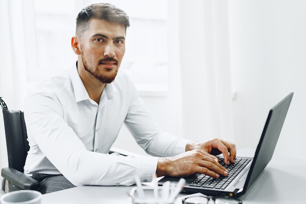 Grave hombre concentrado en silla de ruedas usando su computadora portátil para trabajar / buscar trabajo en internet