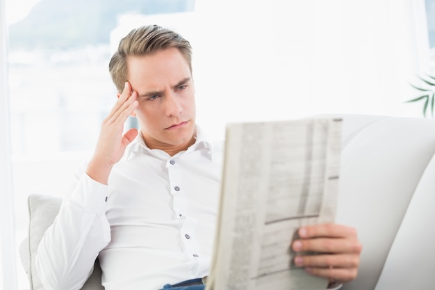 Grave hombre relajado leyendo el periódico en el sofá