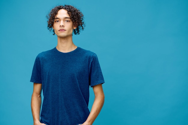 Grave jovem bonito encaracolado bronzeado cara caucasiano em camiseta básica posando isolado sobre fundo azul Conceito de estilo de vida e emoções Boa oferta com espaço de cópia para anúncio