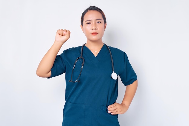 Grave jovem enfermeira asiática vestindo uniforme azul com um estetoscópio mostrando apoio a colegas colegas levantando o punho em gesto de unidade isolado no fundo branco Conceito de medicina de saúde