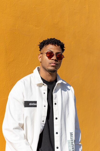 Grave joven afroamericano con gafas de sol rojas retrato sobre fondo amarillo vertical