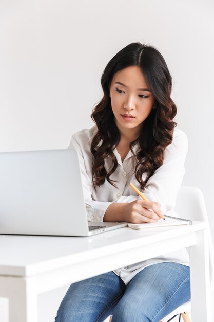 Grave joven empresaria asiática tomando notas