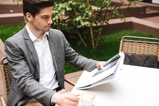 Grave joven empresario vestido con traje tomando café