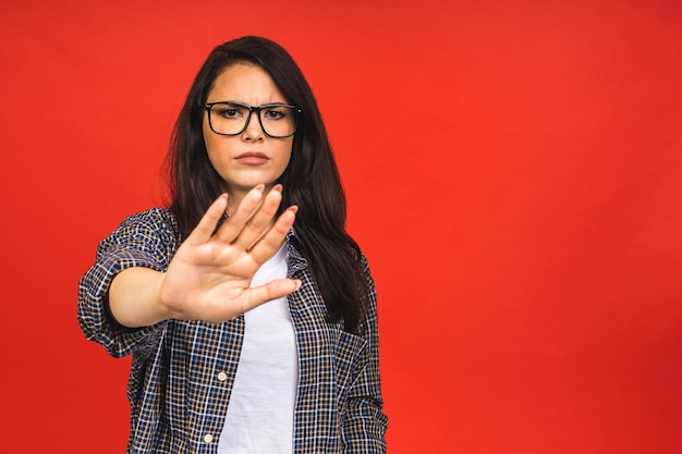 Grave joven hermosa mujer mostrando señal de stop símbolo de prohibición aislado sobre fondo rojo.