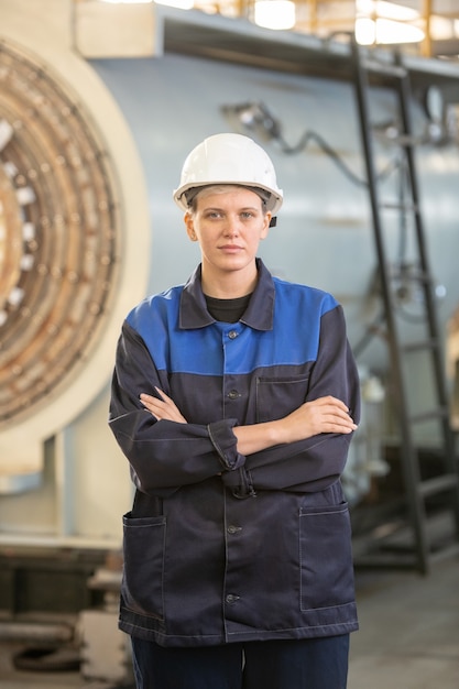 Grave joven operador asiático en casco con computadora de máquina industrial mientras elige configuraciones en el taller