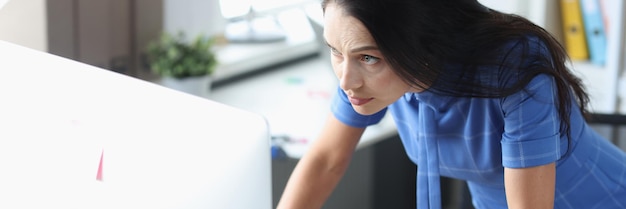 Grave mujer de pie frente a la computadora y mirando el concepto de problemas de trabajo remoto del monitor