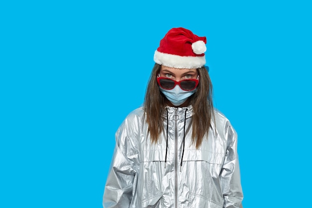 Grave mujer vistiendo gorro de Papá Noel y máscara protectora y gafas de sol rojas