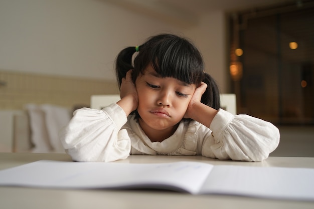 Grave niña estudiante leyendo un libro en casa