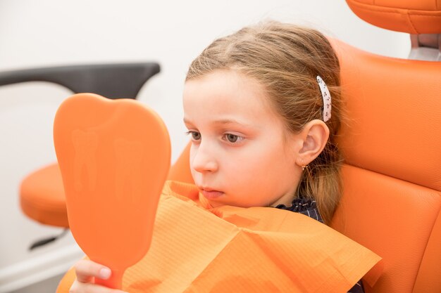 Grave niña mirando el espejo en la silla de dentistas