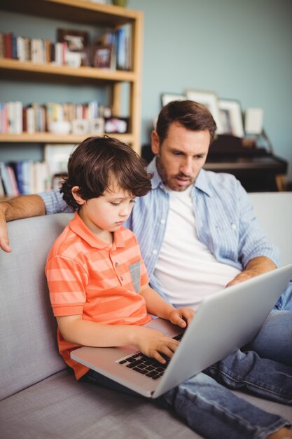 Foto grave padre e hijo usando laptop mientras está sentado en el sofá