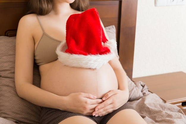 Grávida de chapéu de papai noel segurando a barriga. conceito de natal e ano novo.