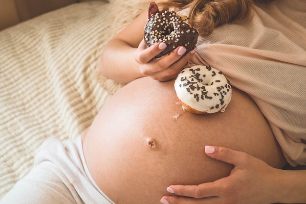 Gravidez e nutrição. mulher grávida apreciando donuts e chá na cama, espaço livre