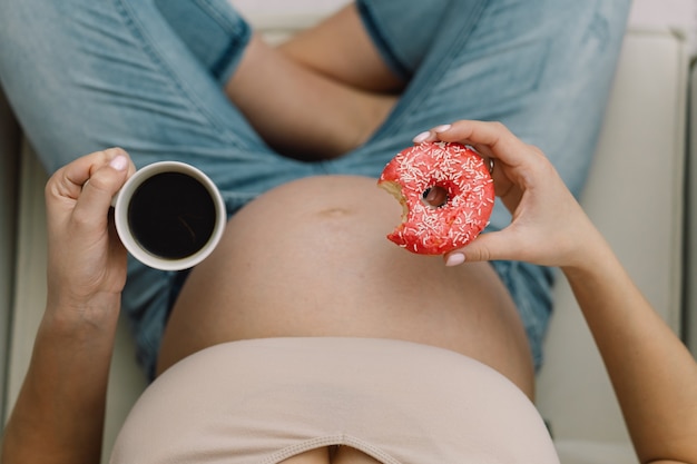 Gravidez e nutrição. Mulher grávida, desfrutando de donuts e chá. Conceito de expectativa e saúde.