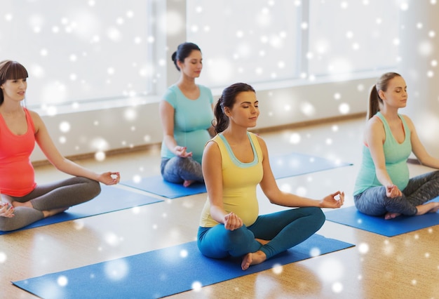 gravidez, esporte, fitness, pessoas e conceito de estilo de vida saudável - grupo de mulheres grávidas felizes exercitando ioga e meditando em pose de lótus no ginásio sobre a neve