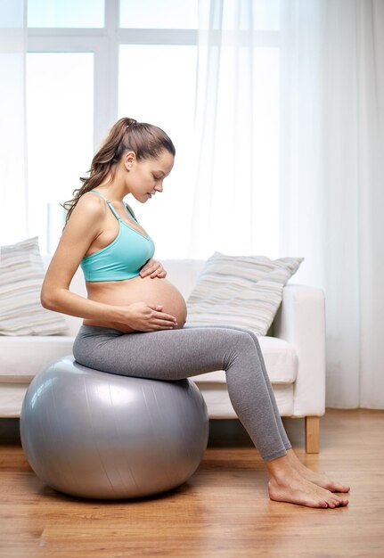 gravidez, esporte, fitness, pessoas e conceito de estilo de vida saudável - mulher grávida feliz se exercitando em fitball em casa