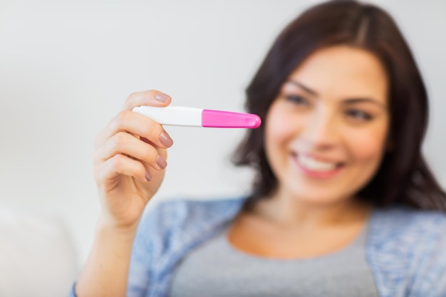 gravidez, fertilidade, maternidade e conceito de pessoas - close-up da mulher sorridente feliz olhando para o teste de gravidez em casa