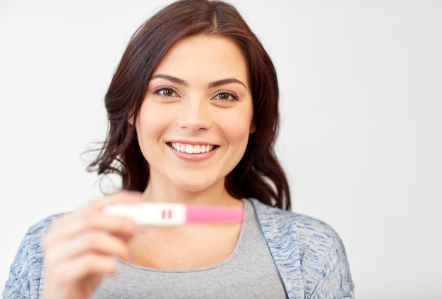 Foto gravidez, fertilidade, maternidade e conceito de pessoas - mulher sorridente feliz segurando e mostrando teste de gravidez em casa positivo