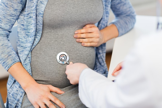 gravidez, ginecologia, medicina, cuidados de saúde e conceito de pessoas - close-up do médico ginecologista com estetoscópio ouvindo batimentos cardíacos de bebê de mulher grávida no hospital