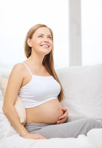 gravidez, maternidade e conceito de felicidade - mulher grávida feliz sentada no sofá e tocando sua barriga e sonhando