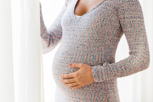 gravidez, maternidade, pessoas e conceito de expectativa - close-up da mulher grávida com barriga grande olhando para a janela