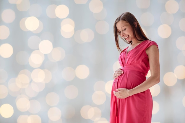 gravidez, maternidade, pessoas e conceito de expectativa - mulher grávida feliz com barriga grande sobre fundo de luzes de férias