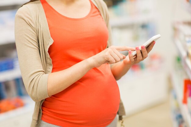 gravidez, medicina, farmacêutica, cuidados de saúde e conceito de pessoas - close-up de mulher grávida com smartphone na farmácia