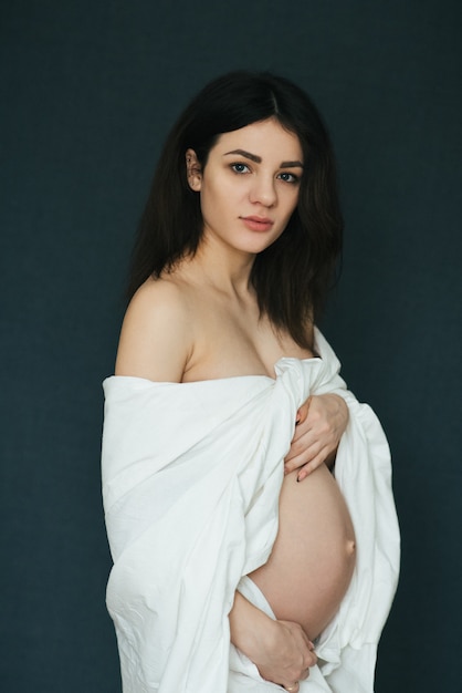Gravidez, menina morena jovem grávida atraente, envolvida em tecido branco