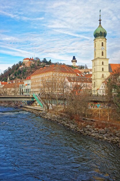 Graz, Österreich - 7. Januar 2014: Flussblick auf die Franziskanerkirche und den Uhrturm des Schlossbergs in Graz in Österreich im Januar