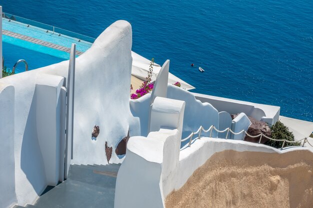 Grécia. dia ensolarado de verão na caldeira vulcânica da ilha de santorini. escada tradicional para o mar. paredes brancas, a beira da piscina azul e um arbusto de flores