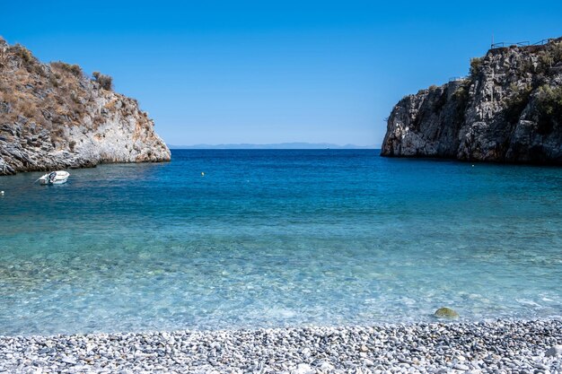 Grécia Praia de seixos barco ancorado em mar calmo Mani Lacônia Peloponeso águas cristalinas