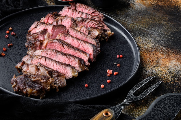 Grelhado ou frito e fatiado carnes marmorizadas costela de olho definido, no prato, com garfo e faca de carne, em mesa rústica escura velha