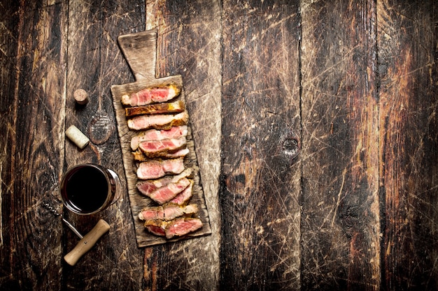 Grelhador de carne. Pedaços de carne de porco grelhada com especiarias e vinho tinto na velha mesa de madeira.