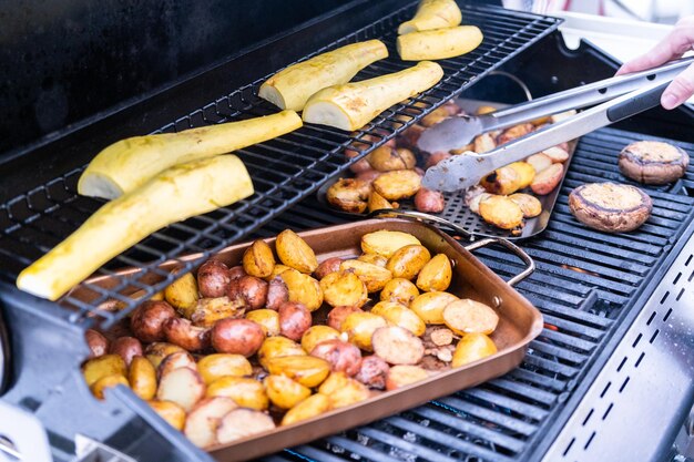 Grelhar batatas pequenas com fatias de alho em uma churrasqueira a gás ao ar livre.