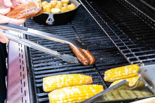 Grelhar cachorros-quentes e legumes frescos em uma churrasqueira a gás ao ar livre no verão.
