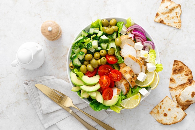 Griechisch inspirierter Salat mit gegrilltem Hühnerfleischgemüse und Feta-Käse in einer Schüssel auf einem Tisch mit Olivenöl-Dressing-Draufsicht