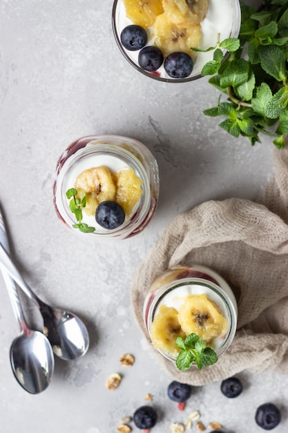 Griechische Joghurtparfaits aus Müsli, Heidelbeeren und Bananen in Einmachgläsern