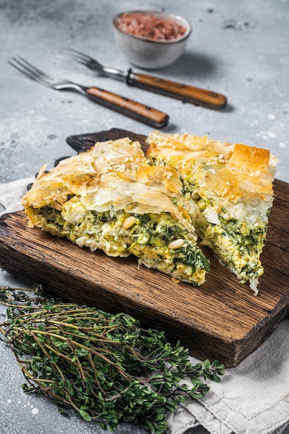 Griechische Torte Spanakopita mit Spinat und Käse auf Holzbrett Grauer Hintergrund Ansicht von oben